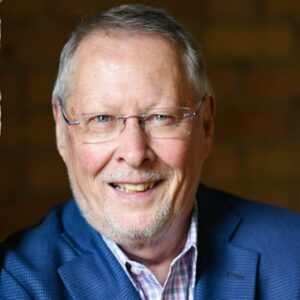 White male with glasses and a smile. Wearing a button up shirt and blue sport coat.